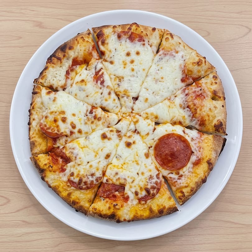Round pepperoni and cheese pizza, sliced and served on a white plate.