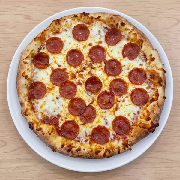 Overhead view of a whole pepperoni pizza on a white plate on a wooden table.